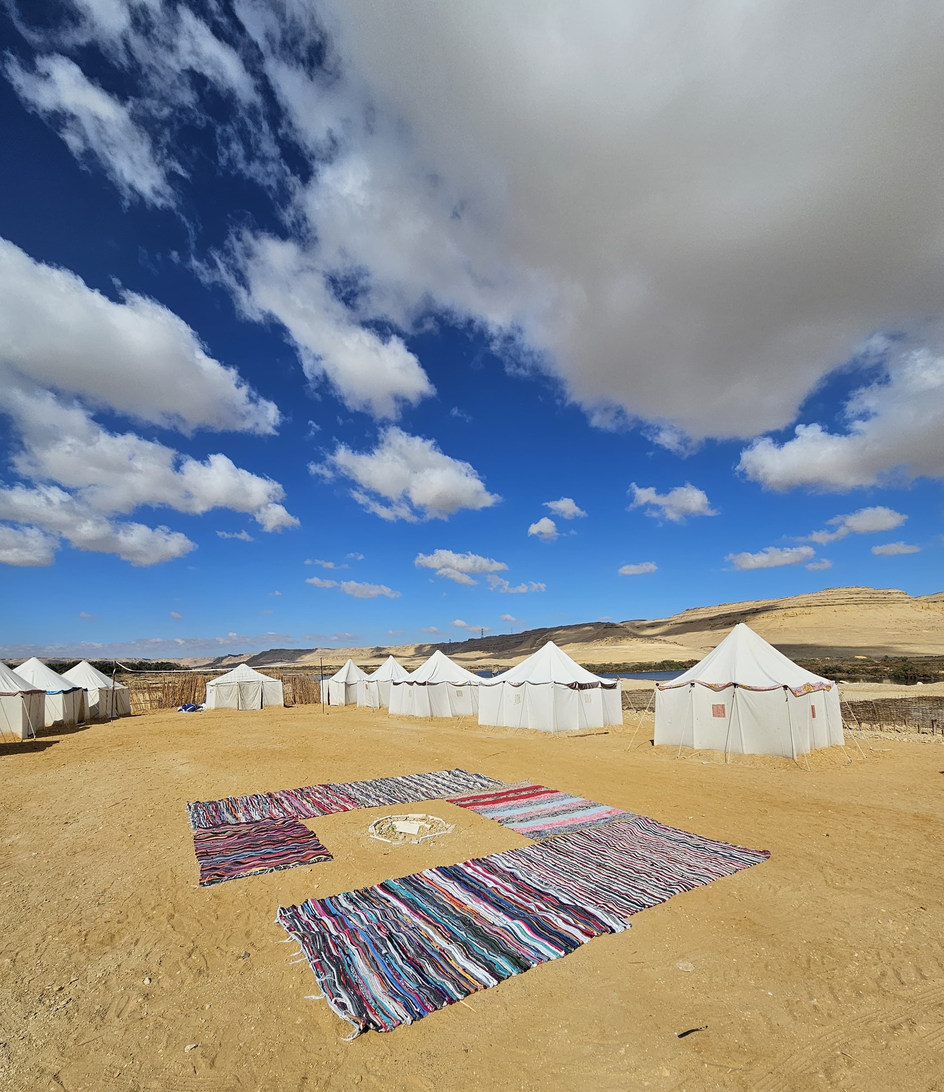 Paisaje desértico con tiendas blancas y alfombras de colores sobre la arena.