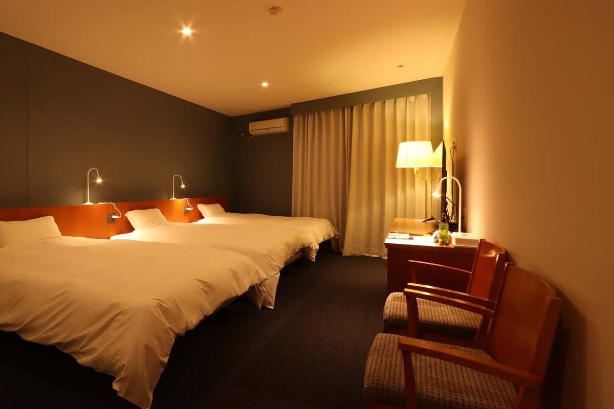 Ein Hotelzimmer mit zwei Betten, einem Schreibtisch mit Stuhl und einer Lampe.