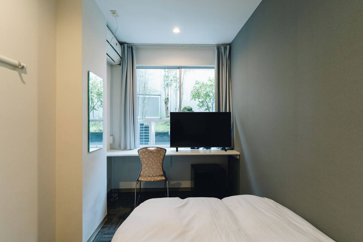 Ein Hotelzimmer mit Bett, Schreibtisch mit Fernseher, Stuhl und einem Fenster mit Vorhängen.
