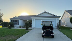 Een woonhuis met garage, oprit en een golfkarretje ervoor geparkeerd.