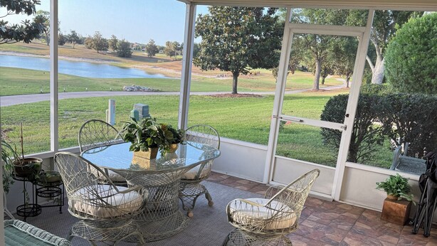 Een overdekt terras met een tafel, stoelen, een plafondventilator en uitzicht op een meer en golfbaan.