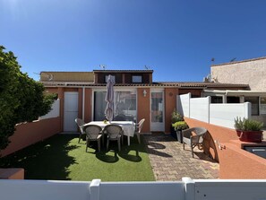 Eine Terrasse mit Tisch und Stühlen, ein kleiner Gartenbereich und ein weißer Zaun.