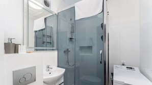 Ein modernes Badezimmer mit einer gläsernen Duschkabine, einem weißen Waschbecken und einem Spiegel.