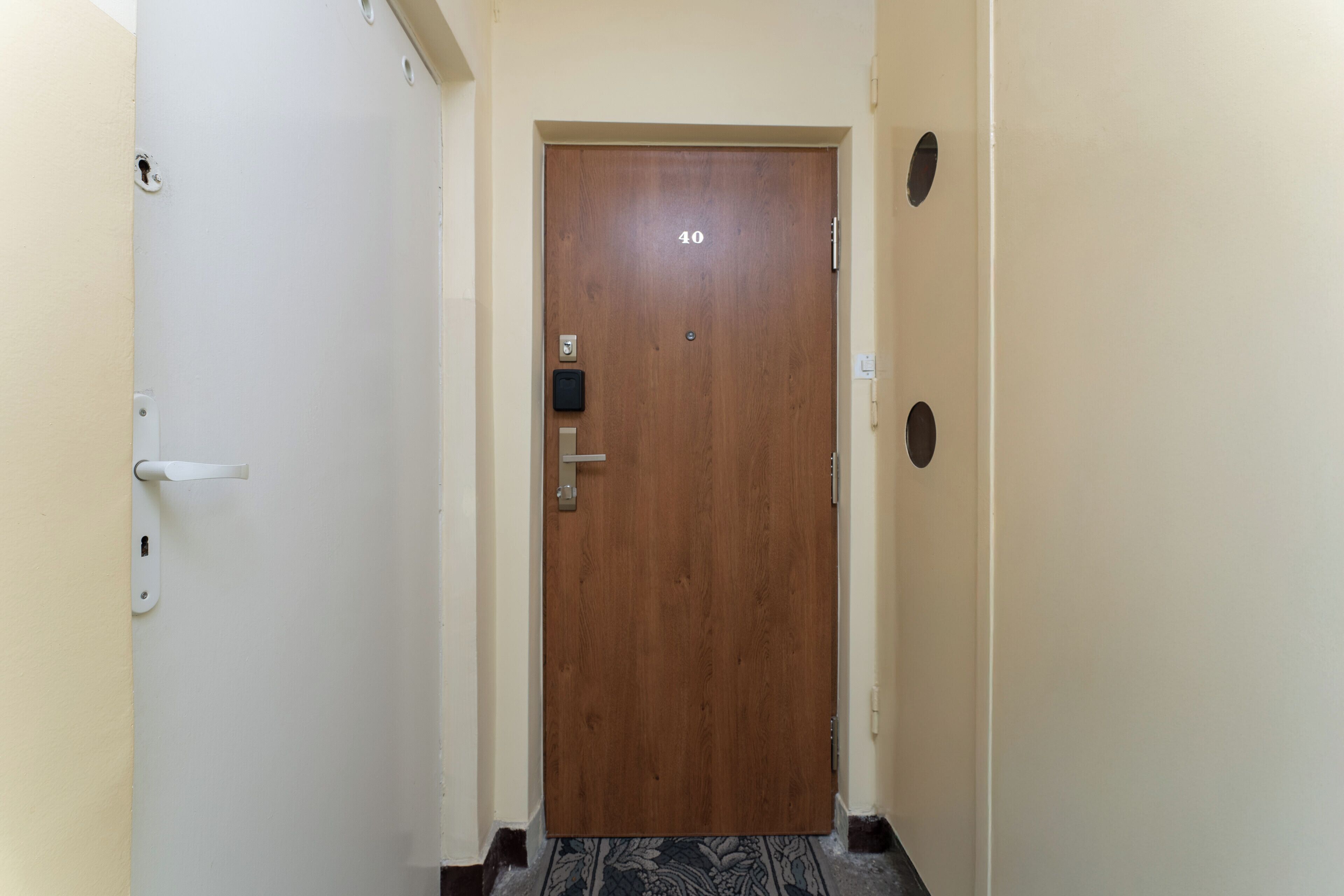 A hallway with a wooden door marked with the number 40, a white door on the left, and a white wall with a small window on the right.