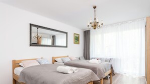 Ein Hotelzimmer mit zwei Holzbetten, einem großen Spiegel, einer Chandelierleuchtre und einem großen Fenster mit durchsichtigen Vorhängen.