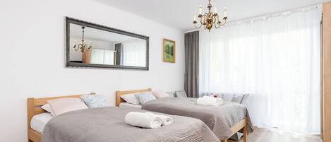 Habitación de hotel con dos camas de madera, un espejo grande, una araña y un amplio ventanal con cortinas de gasa.