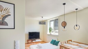 A modern bedroom with a bed, bedside table, TV, and a dining area with a table and chairs. - Słowackiego Avenue Cozy Stay Studio (Kraków)
