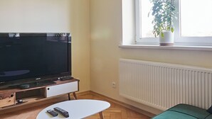 A living room with a flat-screen TV, a green sofa, a white coffee table, and a potted plant by the window. - Słowackiego Avenue Cozy Stay Studio (Kraków)