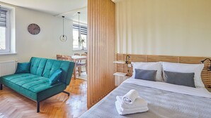 A modern room with a green sofa, a bed with white bedding, and a wooden partition. - Słowackiego Avenue Cozy Stay Studio (Kraków)