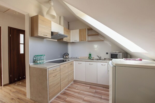 Compact kitchen with microwave, kettle, and sink, featuring light cabinetry and a white countertop.