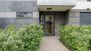 A modern building entrance with a paved pathway flanked by neatly trimmed bushes.