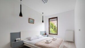 A modern bedroom with a bed, bedside tables, a window, and a radiator.