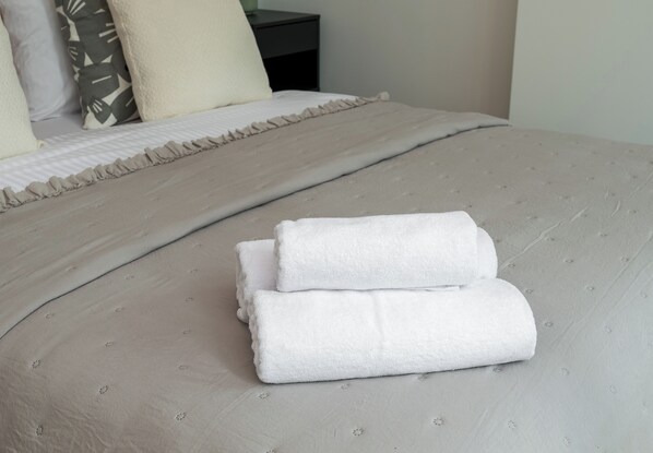 A neatly made bed with a beige duvet and two folded white towels on top.