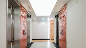 A modern elevator area with metallic doors, a tiled floor, and a plain wall with a ceiling light.