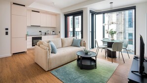 A modern living space with a sofa, a dining table with chairs, a kitchen area, and large windows providing natural light.