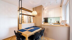 Een compacte keuken met een houten tafel en stoelen, een hanglamp en uitzicht op het aanrecht.