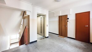 Een hal met een houten deur, een glazen lift en een trap.