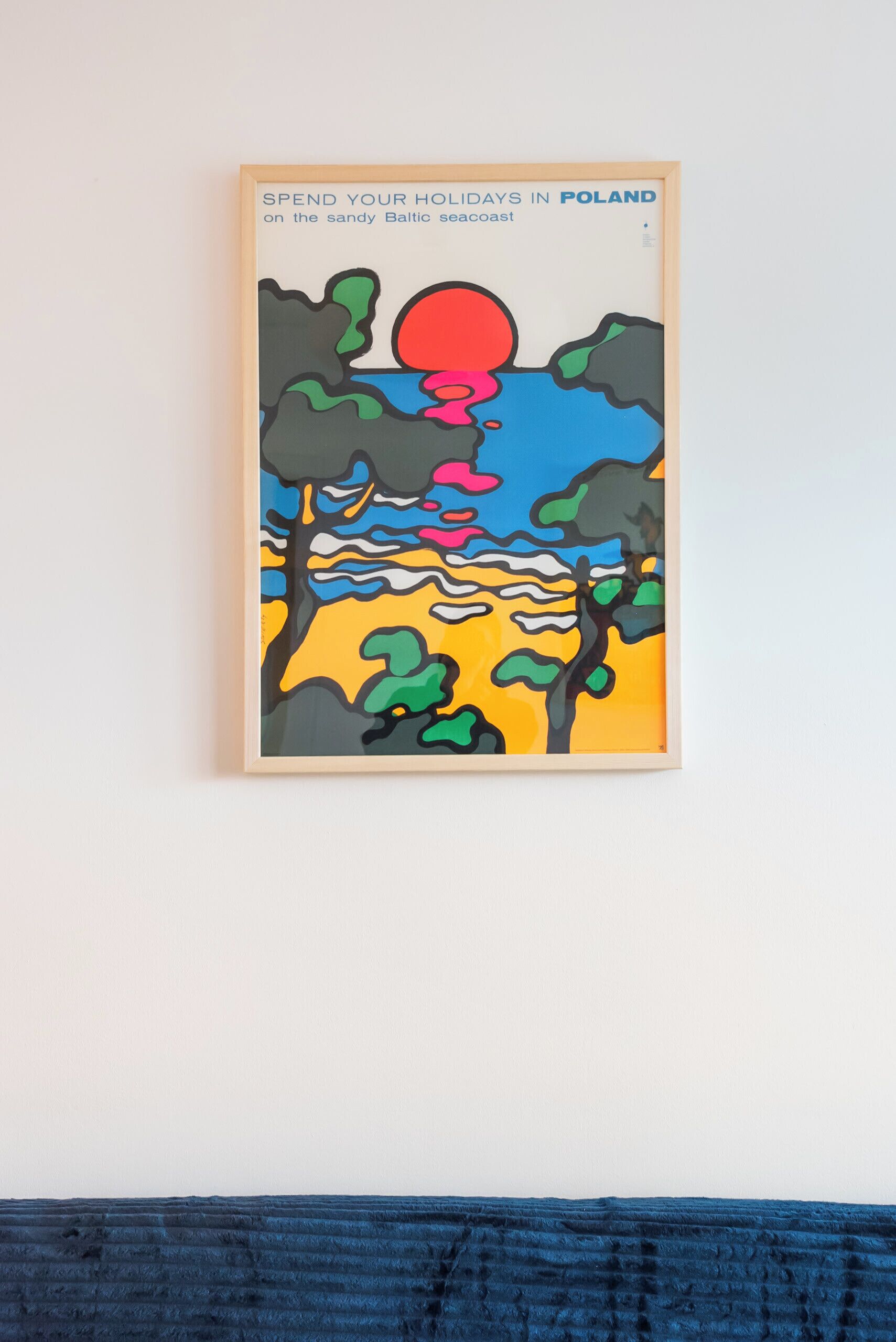 A framed artwork depicting a stylized landscape with a sun, trees, and a body of water.