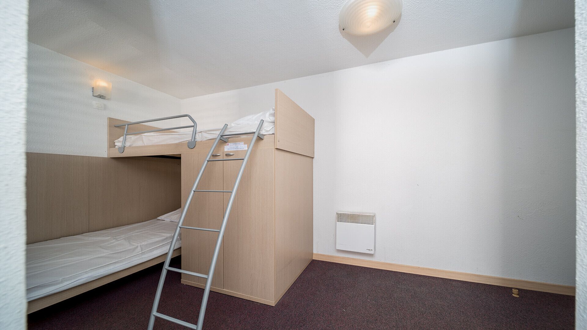 A single bunk bed room with a ladder, a wall-mounted light, and a ventilation unit.
