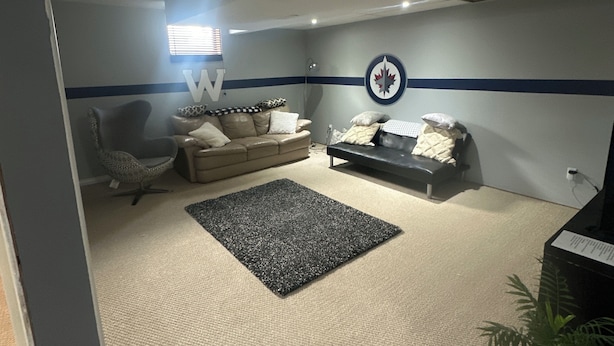 Ein Zimmer mit einer Couch, einem Sessel, einem Teppich und einer Wand mit einem Ahornblatt-Wappen.