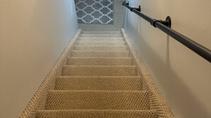 Eine Teppichstufen Treppe mit Handlauf, die zu einem Raum mit einem gemusterten Boden führt.