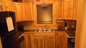 A kitchen with wooden cabinets, a black refrigerator, a sink, and a window with blinds. - Paradise on the Little Red River and prime trout fishing! (Heber Springs)