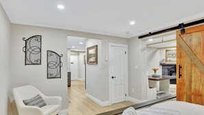 A bedroom with a bed, a chair, a wooden door, and a hallway leading to another room. - Cozy and Chic 1-Bedroom Apartment in Historic Central Denver - Pet Friendly (Denver)
