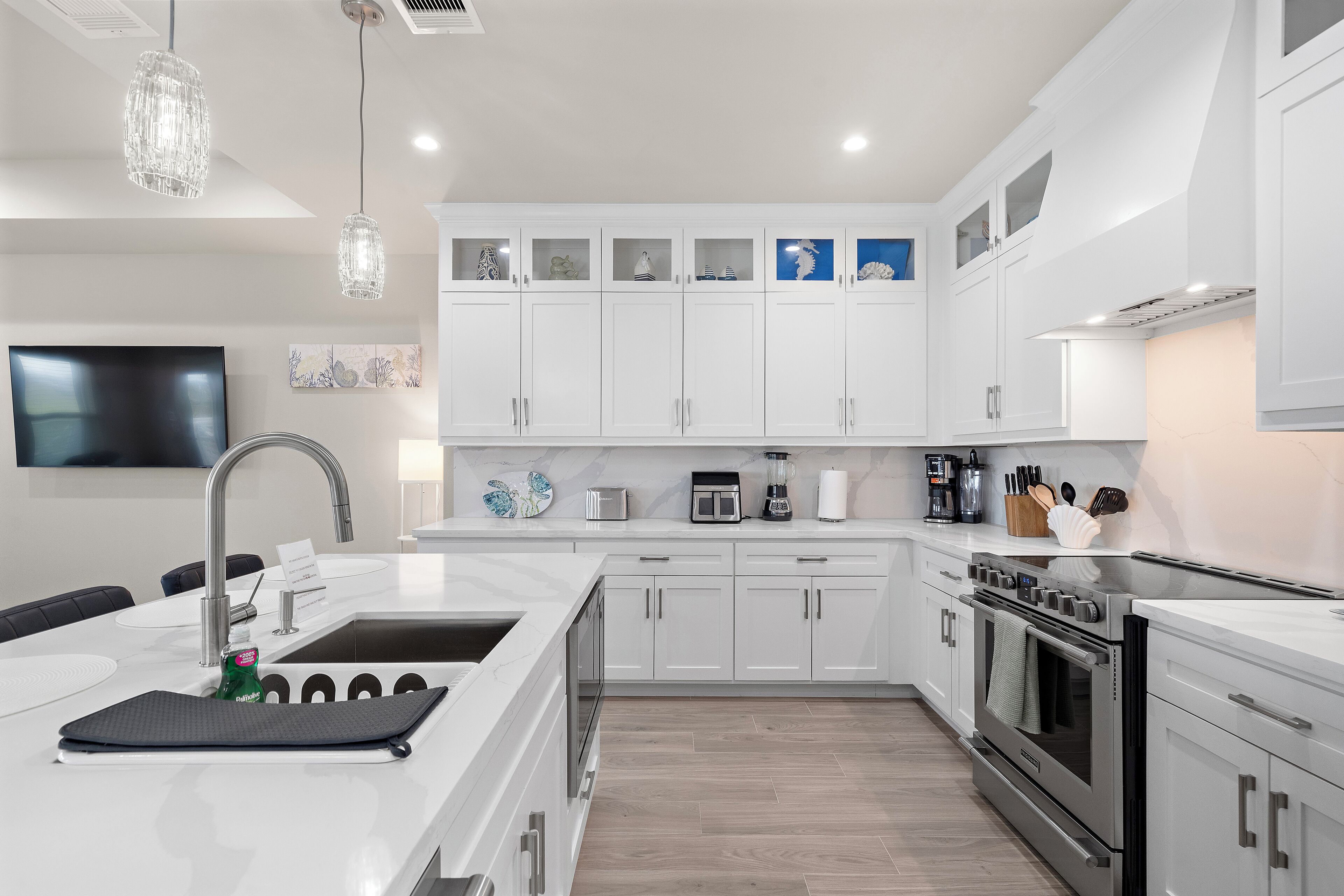 Una cocina moderna con armarios blancos, una isla grande con pileta y electrodomésticos de acero inoxidable, e iluminación colgante.
