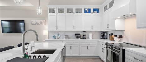 Una cocina moderna con armarios blancos, una isla grande con pileta y electrodomésticos de acero inoxidable, e iluminación colgante.
