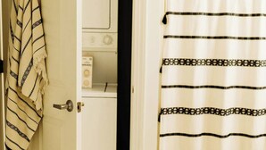 Un bagno con tenda doccia, un asciugamano appeso alla porta e una lavatrice visibile sullo sfondo.