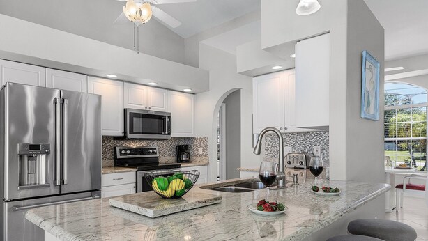A modern kitchen with stainless steel appliances, a marble countertop, and a large island with bar stools. - Heated Pool, Gulf Access & Dock, Pet Friendly - Villa Canal Breeze - Roelens (Cape Coral)