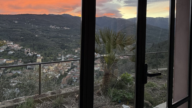 Un balcón con vistas a un pueblo y montañas al atardecer.