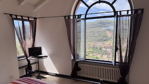 Un dormitorio con un ventanal grande, una cama con colcha a rayas coloridas, un escritorio con una computadora portátil y vistas a un paisaje montañoso.