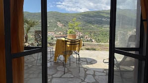 Un balcón con mesa y sillas, con vistas a un paisaje montañoso y un pueblo en la ladera.