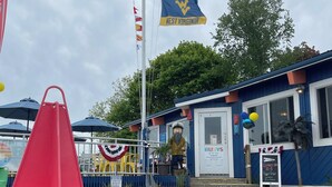 A building with a blue exterior, a flagpole with the American flag and a flag with 'NEST VIRGINIA' on it, and a small statue of a man. - Coastal Living in the heart of St. Ignace. (St. Ignace)