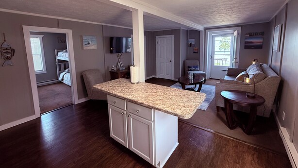 A spacious living area with a kitchen island, a seating area with a sofa and chairs, and a door leading to another room. - Coastal Living in the heart of St. Ignace. (St. Ignace)