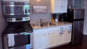 A kitchen with white cabinets, stainless steel appliances, a granite countertop, and a wall-mounted light. - Coastal Living in the heart of St. Ignace. (St. Ignace)