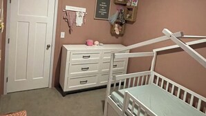 Une chambre de bébé avec un berceau, une commode et un transat fixé au mur.