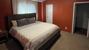 Une chambre avec un grand lit, une table de chevet, une fenêtre avec des stores et une porte.