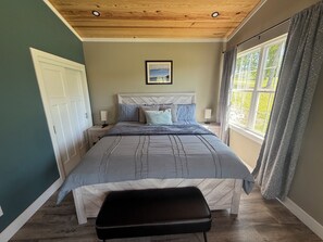 A bedroom with a bed, bedside tables, a window with curtains, and a ceiling with wooden beams.