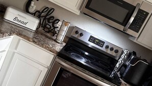 A kitchen with white cabinets, a stainless steel stove, a microwave, and a coffee maker. - Welcome to your home away from home! Our charming 4 bedroom home (Alexander)