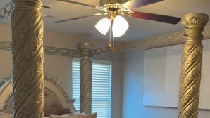 A four-poster bed with ornate columns, a ceiling fan, and two ottomans. - Welcome to your home away from home! Our charming 4 bedroom home (Alexander)