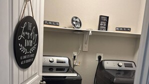 A laundry room with two washers and dryers, a sign that says "The Laundry Room," and a shelf with laundry-related items. - Welcome to your home away from home! Our charming 4 bedroom home (Alexander)