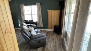 A spacious room with a wooden ceiling, a large window with curtains, a leather sofa, and a wooden cabinet. - Private Cabin on 90 Acres! (Troy)