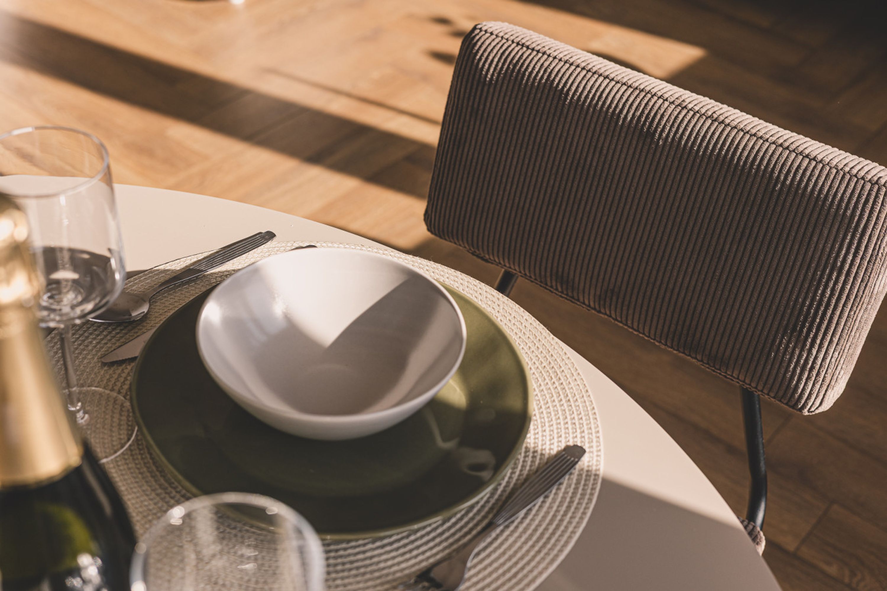 Una mesa de comedor con un bol, una copa de vino y cubiertos.