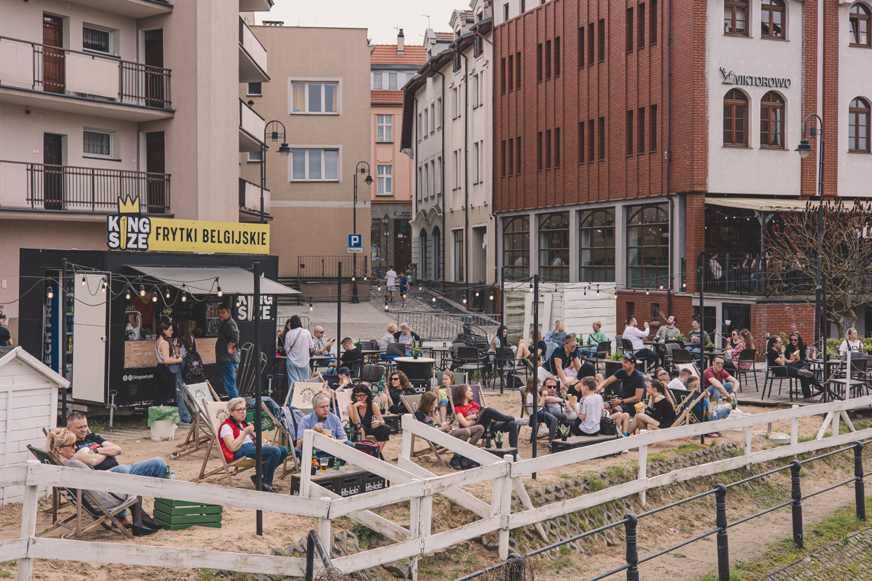 Espaço ao ar livre com mesas e cadeiras, cercado por edifícios com diferentes lojas.