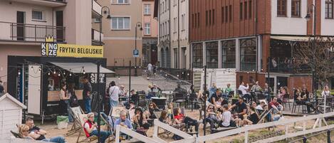 An outdoor seating area with tables and chairs, surrounded by buildings with various storefronts.