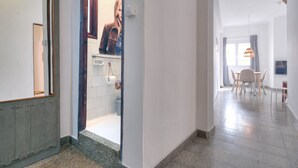 Pasillo que conduce a un baño con rollo de papel higiénico, un espejo y una persona con una chaqueta marrón.