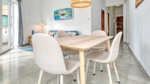 Un comedor con una mesa de madera y cuatro sillas, una lámpara de fibra y un adorno azul en la pared.