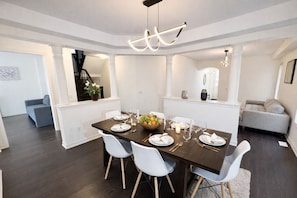 A dining area with a dark wooden table, white chairs, and a fruit bowl centerpiece. - 4BR Group Retreat by Canterra Stays · Sleeps 12 (Brampton)